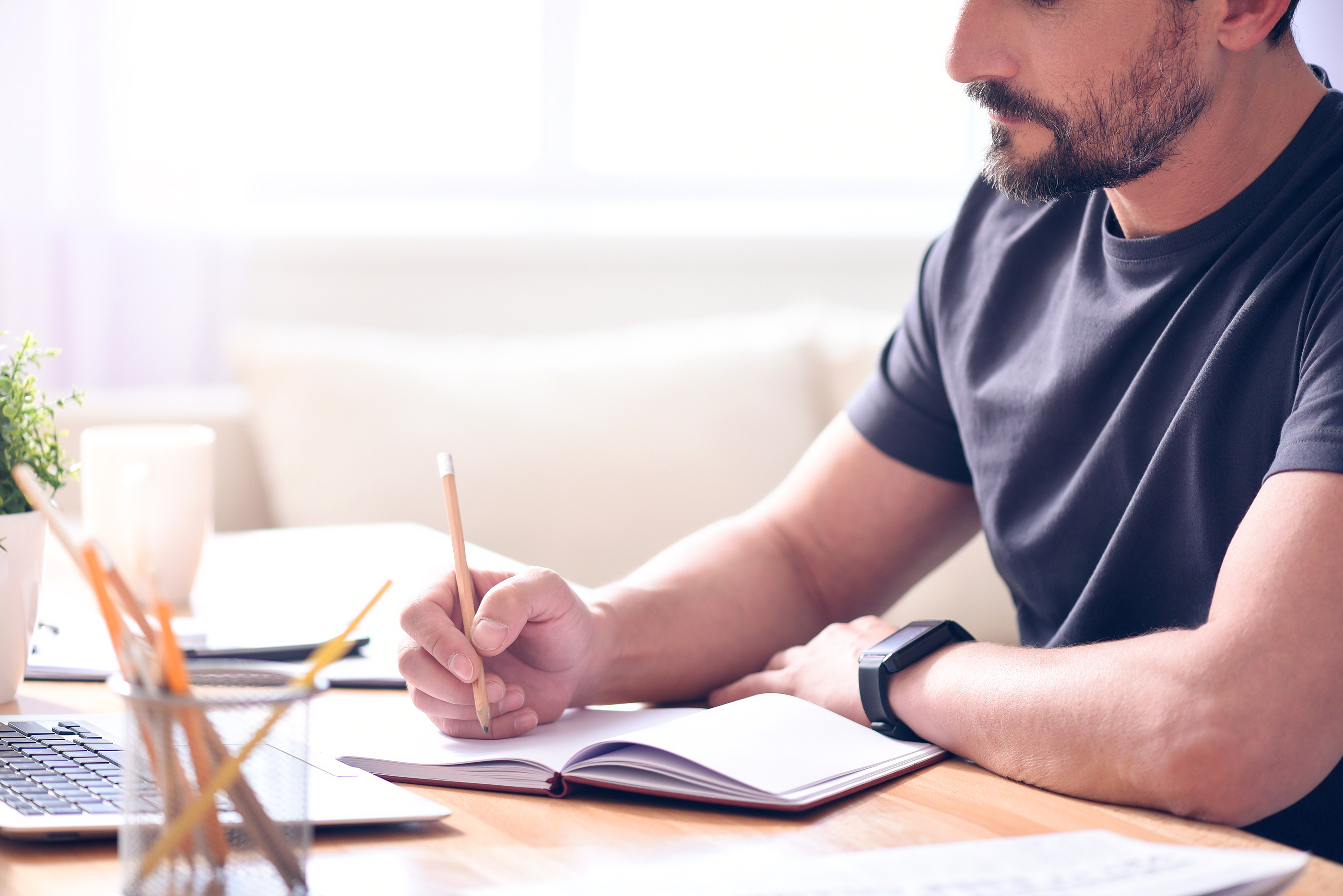 Person taking notes while watching an online course on a laptop, preparing for a consultant interview.