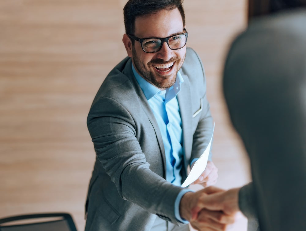 A smiling man in a suit shakes hands with an interviewer, representing a successful outcome from an NHS consultant interview skills course.